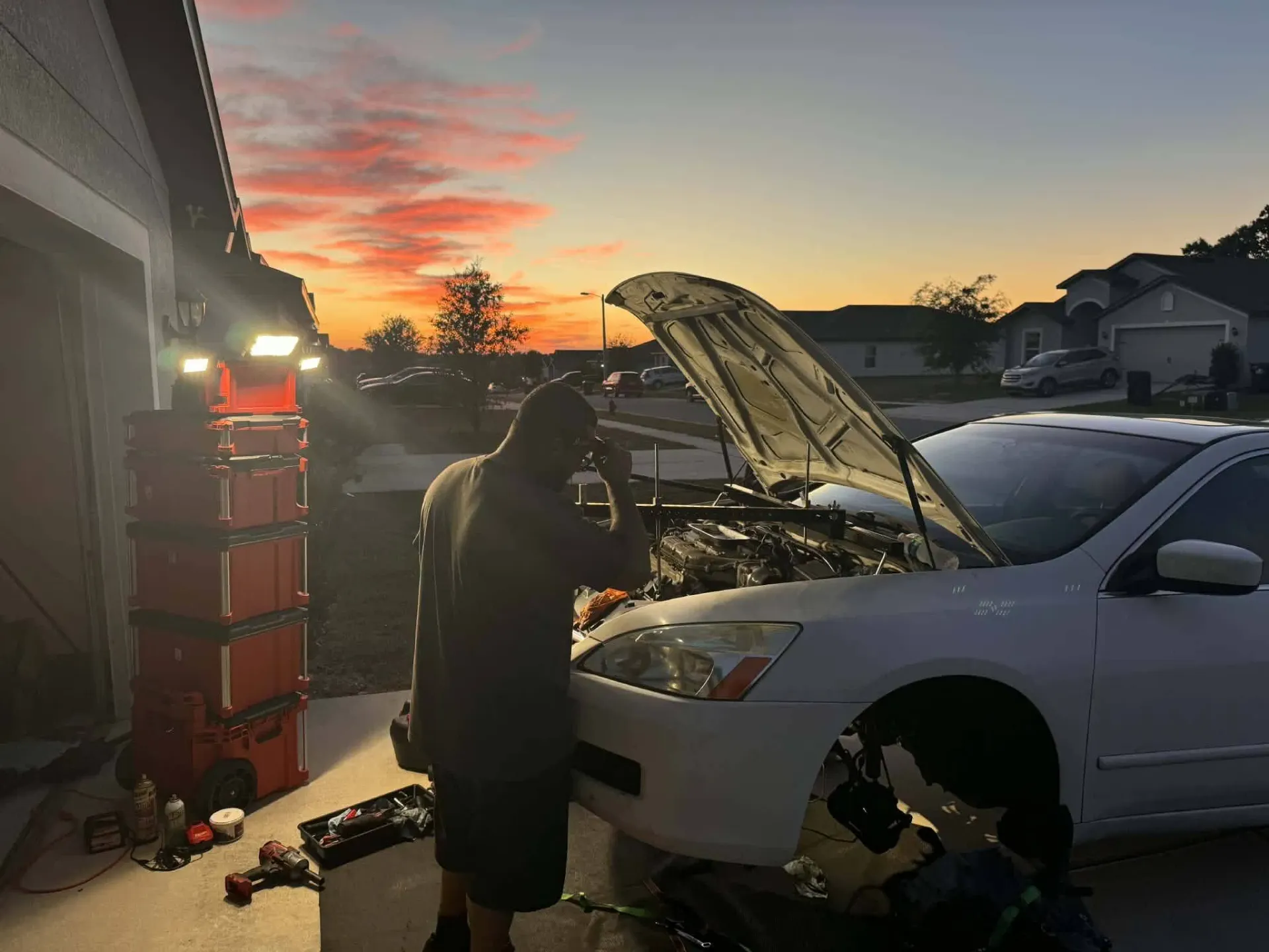 Mobile mechanic performing an engine repair in a driveway at sunset