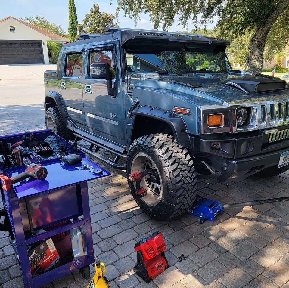 Blue Hummer H2 lifted for maintenance in a driveway with a rolling tool cart